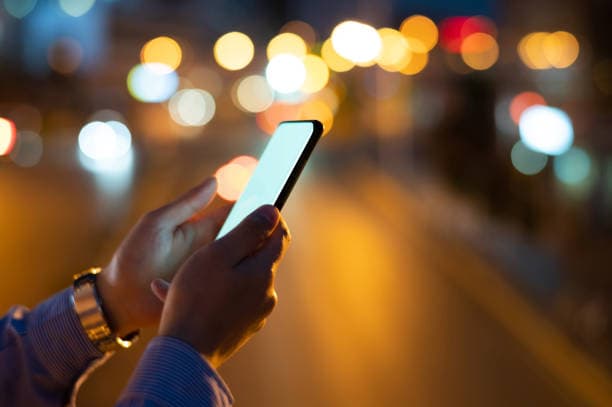 Un parent lit un message sur son téléphone, le soir, dans la rue