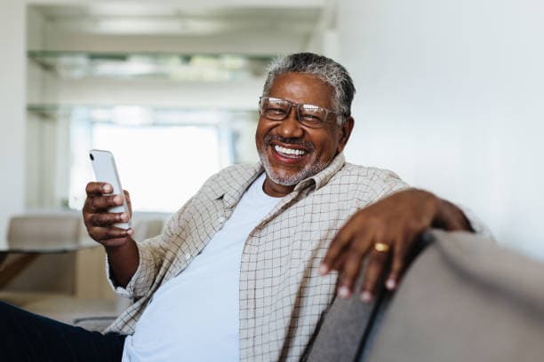 Un parent souriant consulte son téléphone, assis dans son salon